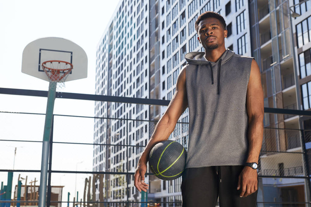 Retrato de jogador de basquete afro-americano em pé olhando para a câmera na quadra ao ar livre, espaço de cópia
 - Foto, Imagem