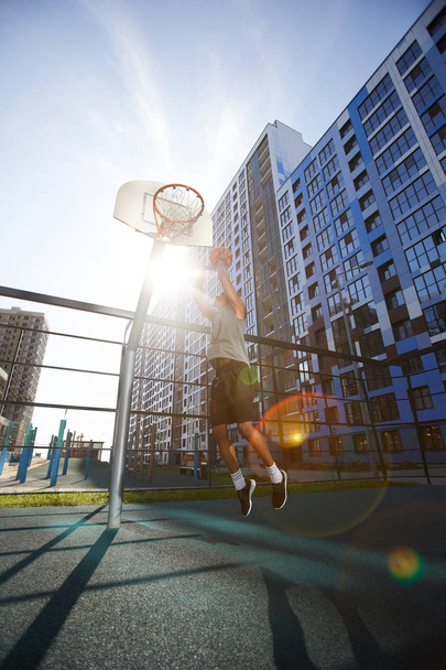 Action shot of African basketball player shooting slam dunk in outdoor court, lens flare - Photo, Image