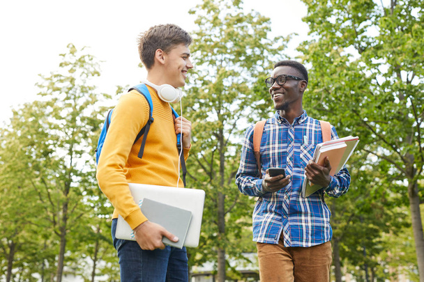 Портрет улыбающегося афроамериканского студента, разговаривающего с другом во время прогулки по университетскому городку, копирующего пространство
 - Фото, изображение
