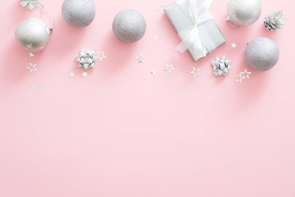 Christmas decorations, stylish silver gift box, baubles, pine cones, confetti on pastel pink background. Minimal flat lay style composition, top view, copy space. Christmas fashion glamour concept. - Valokuva, kuva