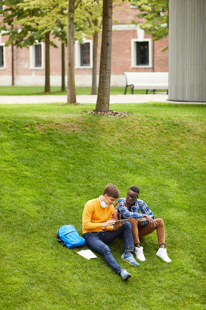 Pełna długość Portret dwóch studentów siedzi na zielonym trawniku w kampusie i za pomocą cyfrowego tabletu, Kopiuj przestrzeń - Zdjęcie, obraz