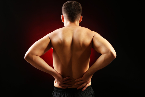 νεαρός άνδρας με πόνο στην πλάτη, σε κόκκινο φόντο - Φωτογραφία, εικόνα