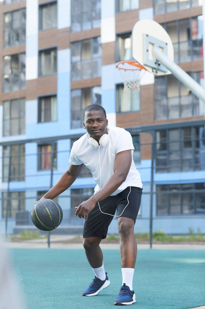 屋外のカメラに向かって移動するアフリカのバスケットボール選手のフルレングスアクションショット - 写真・画像