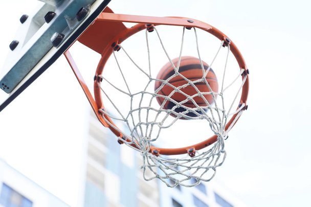 Крупный план баскетбольной стрельбы через обруч на городском фоне, копировальное пространство
 - Фото, изображение