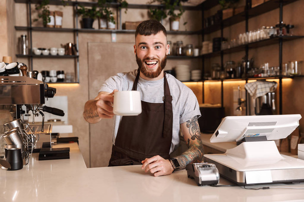 Smiling attractive man barista standing - Фото, изображение
