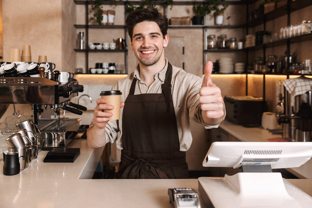 schöner glücklicher Kaffeemensch posiert in der Cafébar, die drinnen arbeitet und eine Kaffeetasse hält. - Foto, Bild