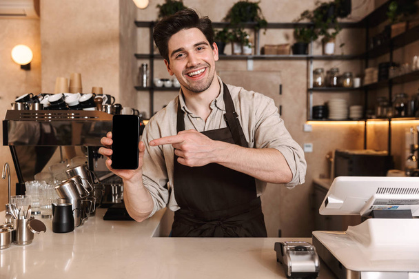 Happy coffee man posing in cafe bar working indoors showing display of mobile phone. - Fotoğraf, Görsel