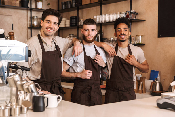 Three cheerful male baristas standing at the coffee shop - Zdjęcie, obraz