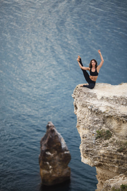 Kaunis hoikka nainen harjoittaa joogaa ja pilates kalliolla vuoren merinäköalalla. Urheilullinen ja terveellinen elämäntapa käsite
. - Valokuva, kuva