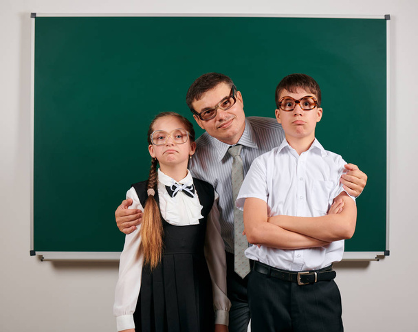 Portrait of a teacher, schoolboy and schoolgirl with old fashioned eyeglasses posing on blackboard background - back to school and education concept - Photo, Image