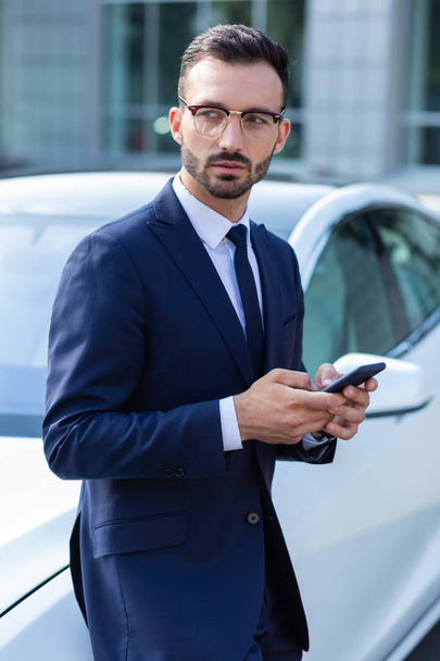 Bearded businessman texting wife while waiting for her near car - Zdjęcie, obraz