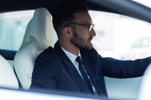 Prosperous businessman feeling thoughtful while driving car - Foto, imagen