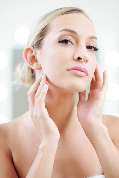 Beautiful young woman applying moisturizing lotion and doing light face massage - Foto, Imagen