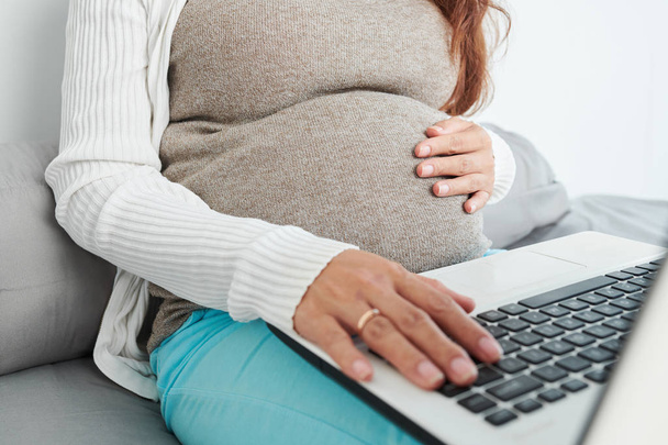 Close-up image of pregnant woman touching her baby kicking in womb and searching for information on laptop - Photo, Image