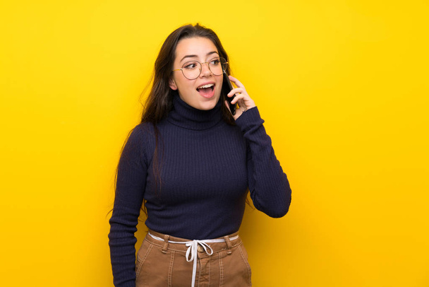 Девушка-подросток над изолированной желтой стеной поддерживает разговор с мобильным телефоном
 - Фото, изображение