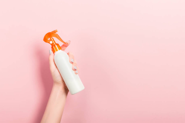 Samičí ruční stříkací láhev z mléka izolovaná. Dívka dává kosmetické prostředky na růžovém pozadí - Fotografie, Obrázek