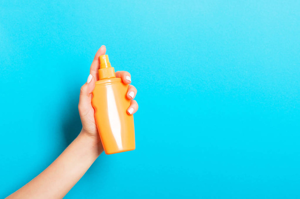 Female hand holding spray cream bottle of lotion isolated. Girl give cosmetic products on blue background - Valokuva, kuva