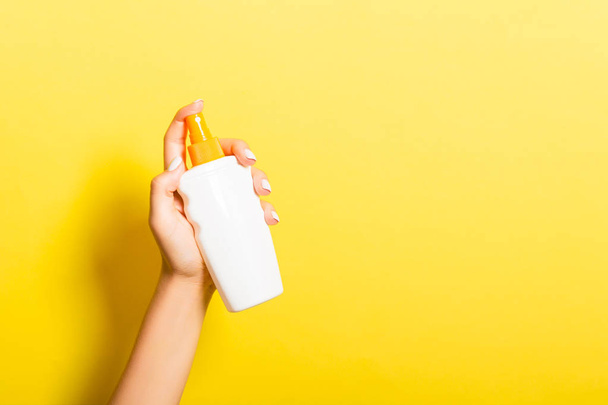Женская рука, держащая бутылку лосьона с кремом от спрея изолированы. Девушка дает косметические средства на желтом фоне
 - Фото, изображение