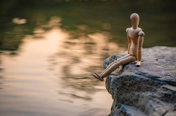 Articulated little man sitting on a stone by the river - Photo, Image