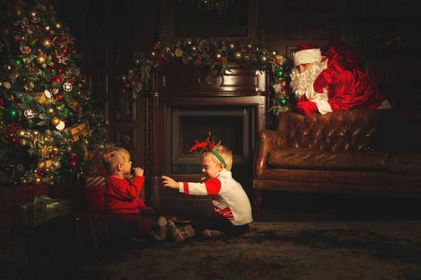 Kinder spielen in der Nähe des Weihnachtsbaums. der wirkliche Weihnachtsmann ist w - Foto, Bild