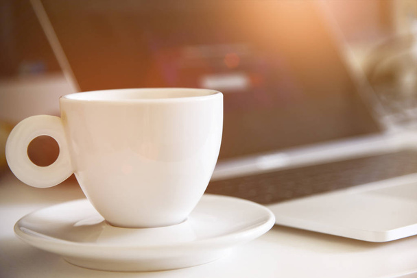 İş için bir fincan kahve ve laptop. Seçici olarak kahveye odaklan. Güneş efekti tarzı resim - Fotoğraf, Görsel