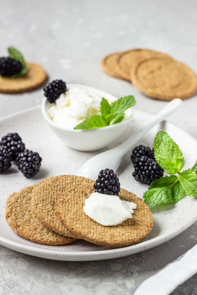 Thin crispy wholegrain crackers with cream cheese, blackberry and mint on a grey plate.  - Fotó, kép