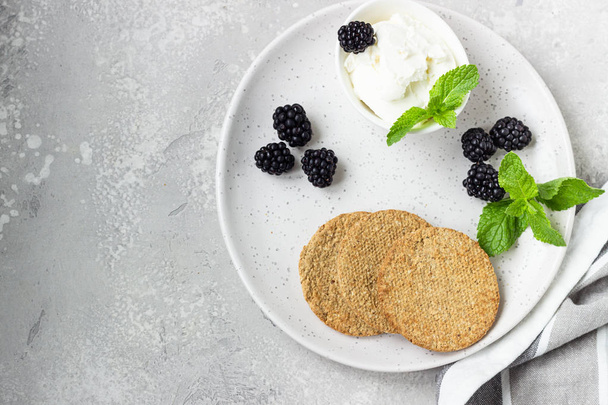 Thin crispy wholegrain crackers with cream cheese, blackberry and mint on a grey plate.  - Fotó, kép