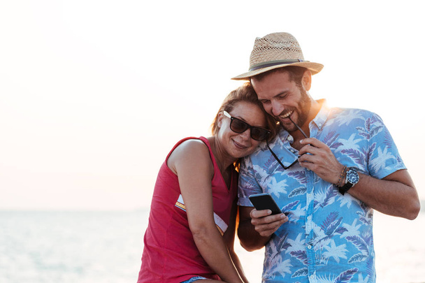 Joven pareja feliz utilizando el teléfono inteligente junto al mar
 - Foto, imagen