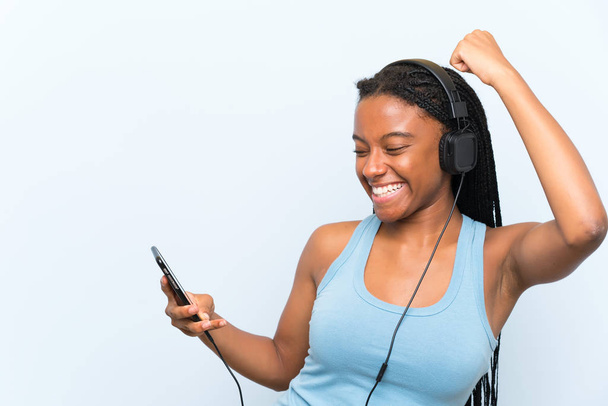 Adolescente afroamericana con el pelo largo trenzado escuchando música con un móvil y bailando
 - Foto, imagen