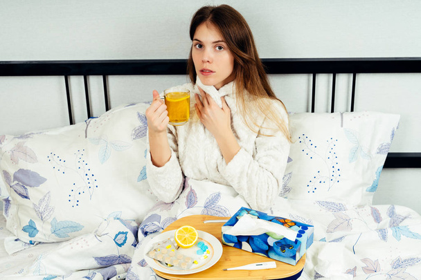 Fiatal nő ül az ágyon, sok gyógyszert az ágyon asztaliten - Fotó, kép