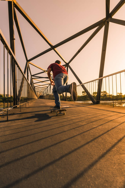 Young skateboarder on bridge at sunset - Fotó, kép