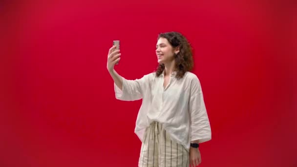 curly girl plays games on an iPhone 11pro in a hand on a red background - Imágenes, Vídeo