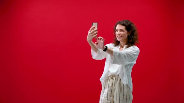 curly girl plays games on an iPhone 11pro in a hand on a red background - Materiał filmowy, wideo