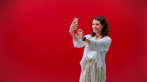curly girl plays games on an iPhone 11pro in a hand on a red background - 映像、動画