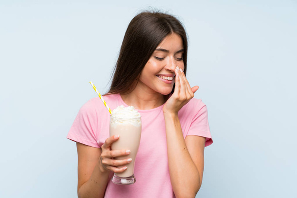 Young woman with strawberry milkshake over isolated blue background smiling a lot - Photo, Image