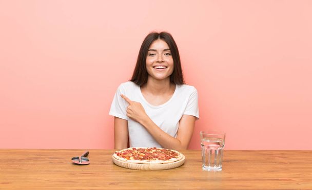Giovane donna con una pizza che punta al lato per presentare un prodotto
 - Foto, immagini