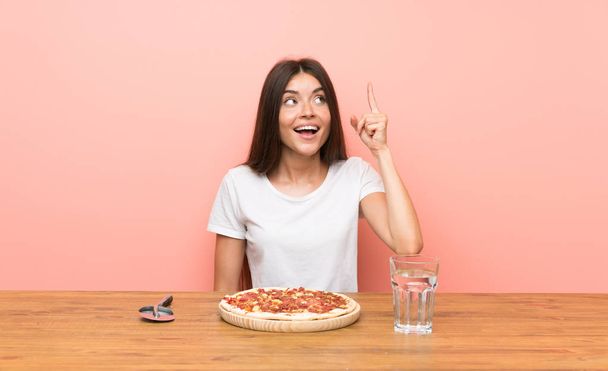 指を持ち上げながら解決策を実現しようとするピザを持つ若い女性 - 写真・画像