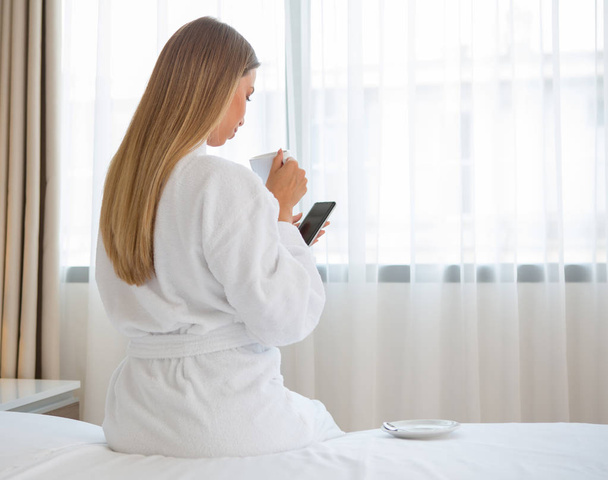 Beautiful woman sitting on the bed enjoying morning coffee  - Фото, изображение