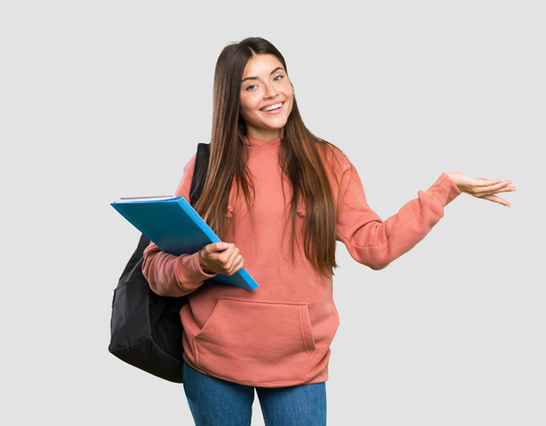 Young student woman holding notebooks extending hands to the side for inviting to come over isolated grey background - Photo, Image