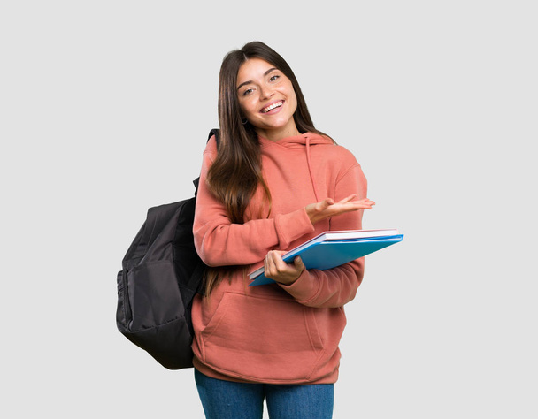 Young student woman holding notebooks presenting an idea while looking smiling towards over isolated grey background - Photo, Image