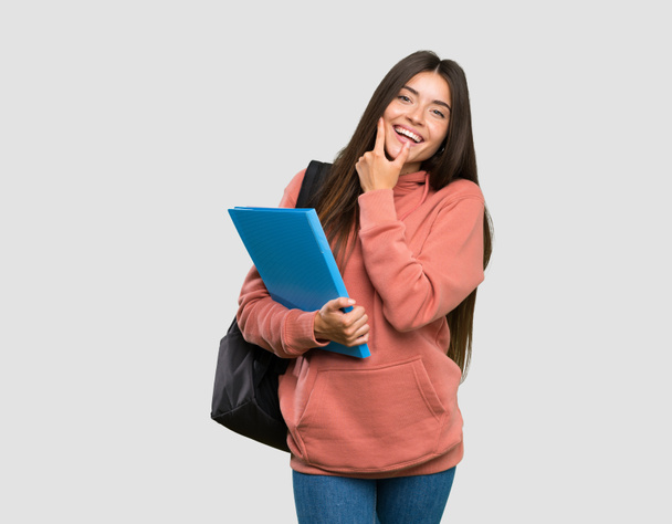 Jonge student vrouw houdt notebooks glimlachend over geïsoleerde grijze achtergrond - Foto, afbeelding