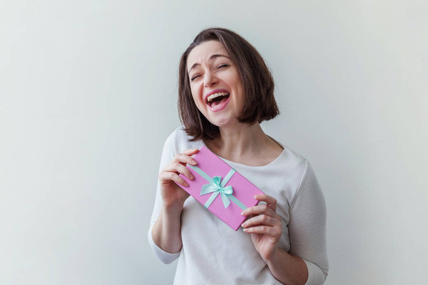 Young positive woman holding small pink gift box isolated on white background. Preparation for holiday. Girl looking happy and excited - Foto, Imagen