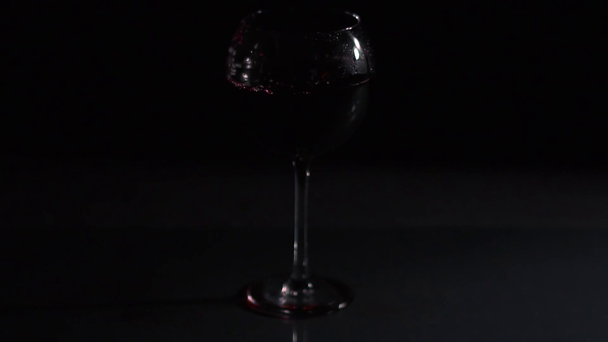 Ice cube falls into a glass of wine on dark background, video  - Footage, Video