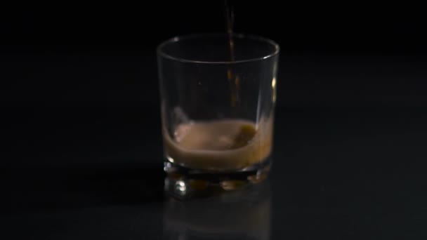 Cola pours into an empty glass. Glass with cola on a dark background. Air bubbles in a glass of cola. Close-up. Black background. - Materiał filmowy, wideo