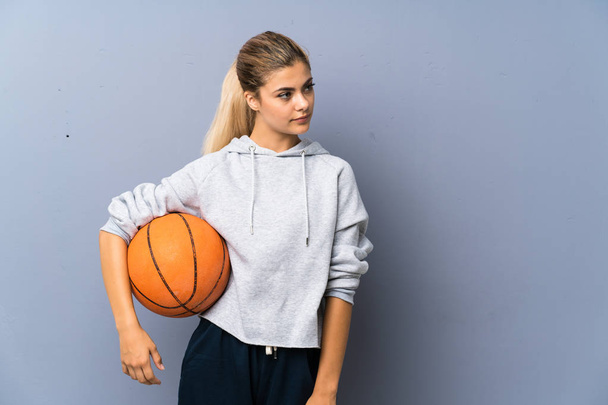 Teenager girl playing basketball over grey wall - 写真・画像