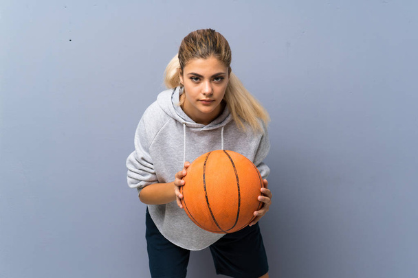 Teenager girl playing basketball over grey wall - 写真・画像
