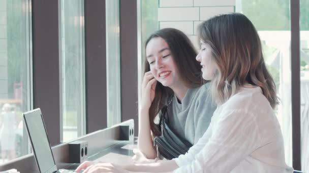 Dos mujeres jóvenes que estudian juntas en la cafetería del campus usando una computadora portátil
 - Imágenes, Vídeo