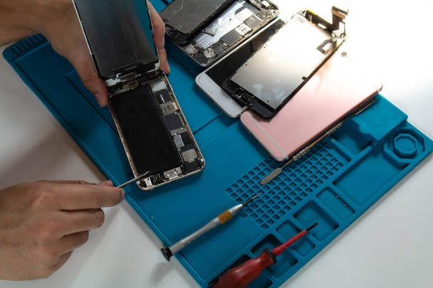 Na mesa de um reparador de celular Ele está atualmente removendo a bateria do telefone celular para substituí-lo com o antigo que se deteriorou em uso
. - Foto, Imagem