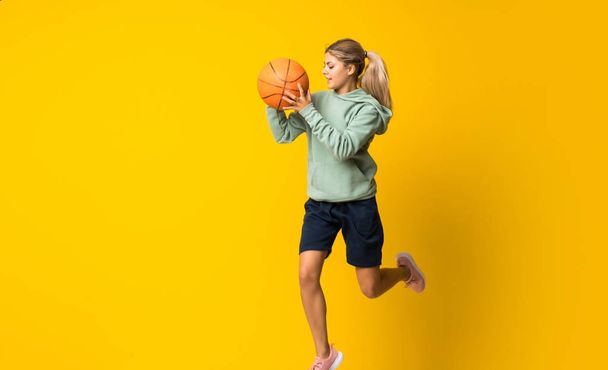Έφηβο κορίτσι μπάσκετ μπάλα άλμα πάνω από απομονωμένο κίτρινο φόντο - Φωτογραφία, εικόνα