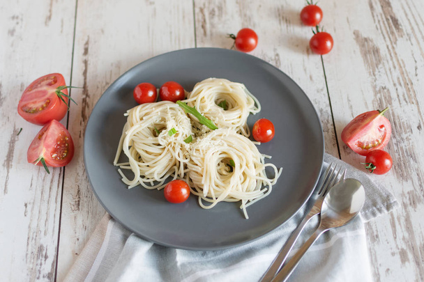 Italian pasta spaghetti nests on a white porcelain plate with tomatoes, parmesan and leves of arugula. - Photo, Image